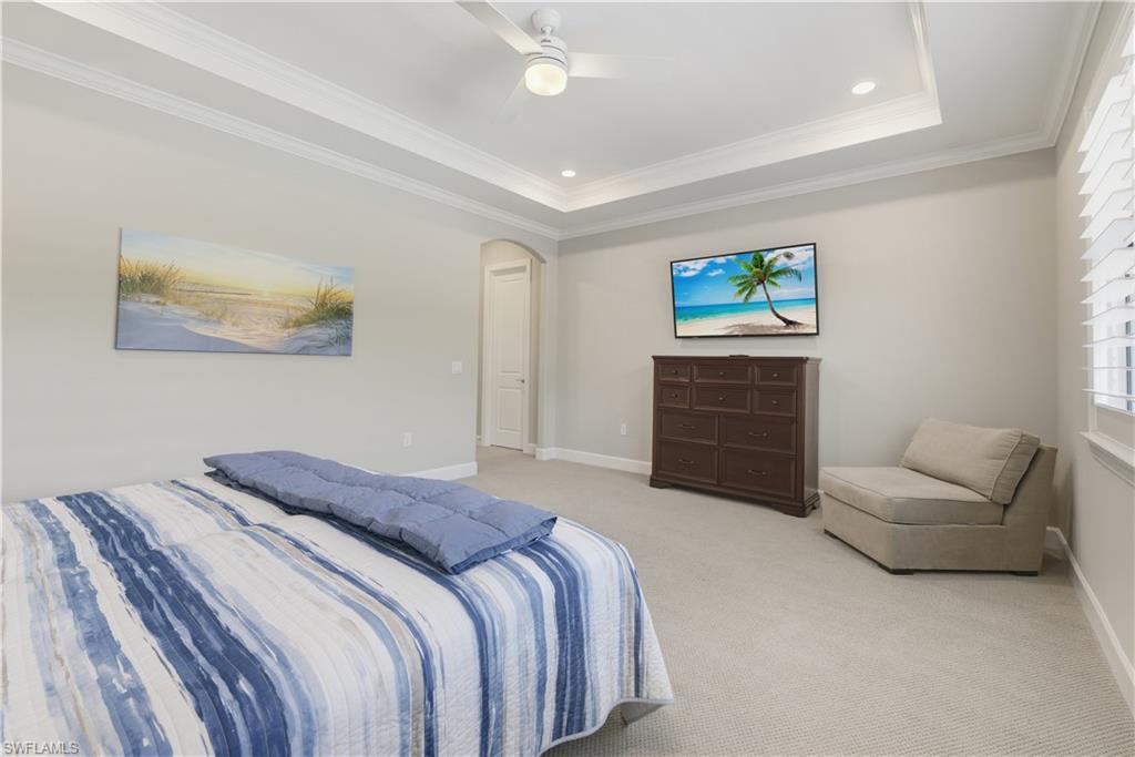 Carpeted bedroom featuring arched walkways, a raised ceiling, crown molding, recessed lighting, and a ceiling fan