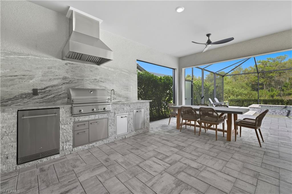 View of patio / terrace with an outdoor kitchen, a sunroom, a ceiling fan, an in-ground hot tub, and outdoor dining area