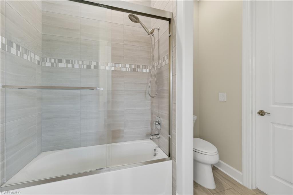 Full bath featuring combined bath / shower with glass door and toilet