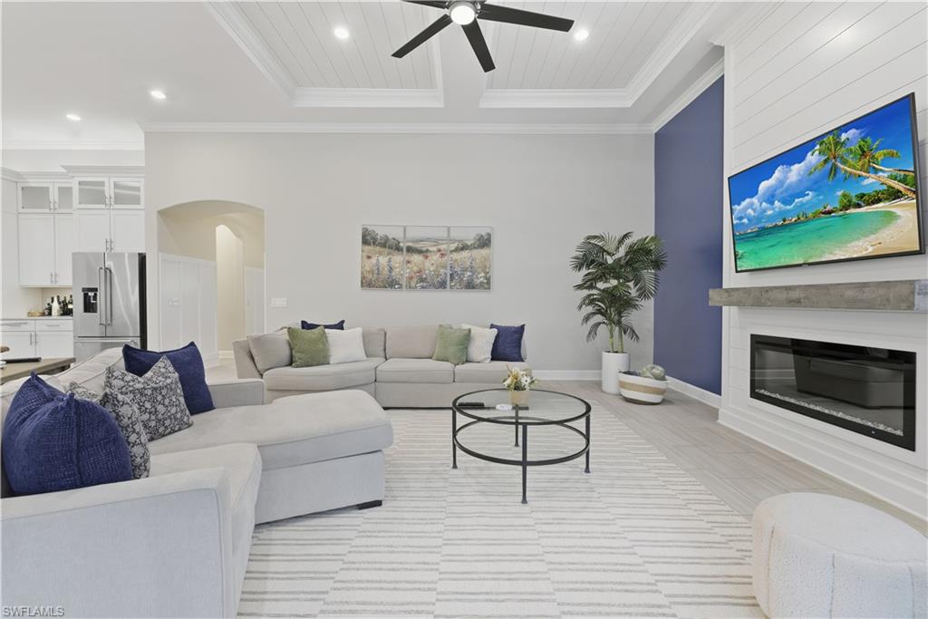 Living area with arched walkways, a glass covered fireplace, recessed lighting, light wood finished floors, and crown molding