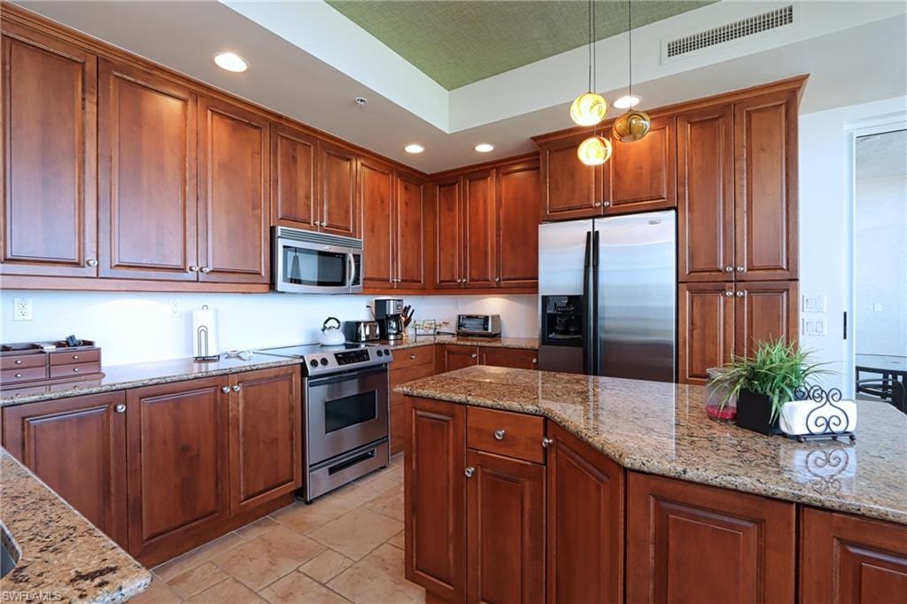 Kitchen with appliances with stainless steel finishes, light tile patterned floors, light stone countertops, and hanging light fixtures