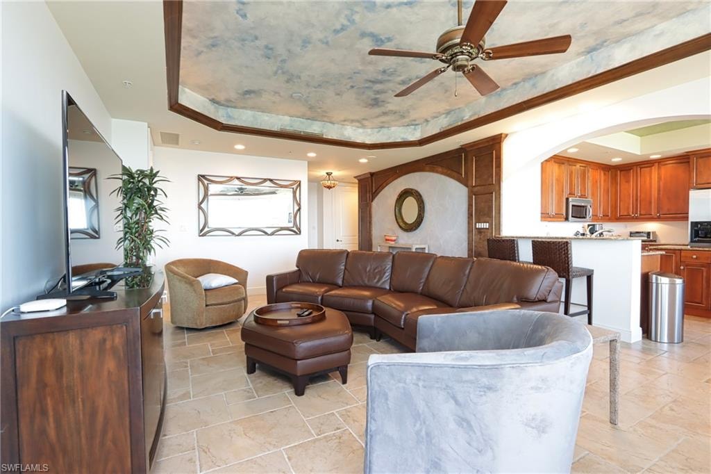 Living room with ceiling fan, light tile patterned floors, and a raised ceiling