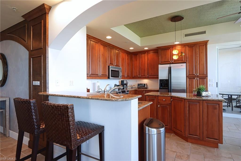 Kitchen featuring hanging light fixtures, light tile patterned floors, light stone countertops, stainless steel appliances, and ceiling fan