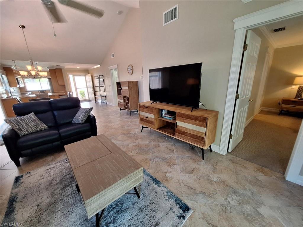 Carpeted living room with high vaulted ceiling and ceiling fan with notable chandelier and HDTV.