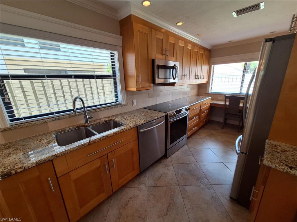 Upgraded Kitchen with light stone countertops, light tile flooring, backsplash, sink, and appliances with stainless steel finishes