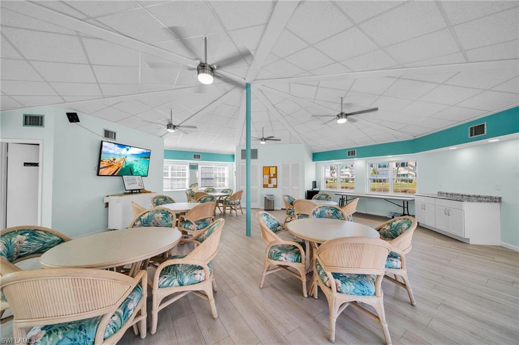 Spacious recreation room featuring a vaulted ceiling with multiple ceiling fans, wood-finish flooring, and a large wall-mounted display