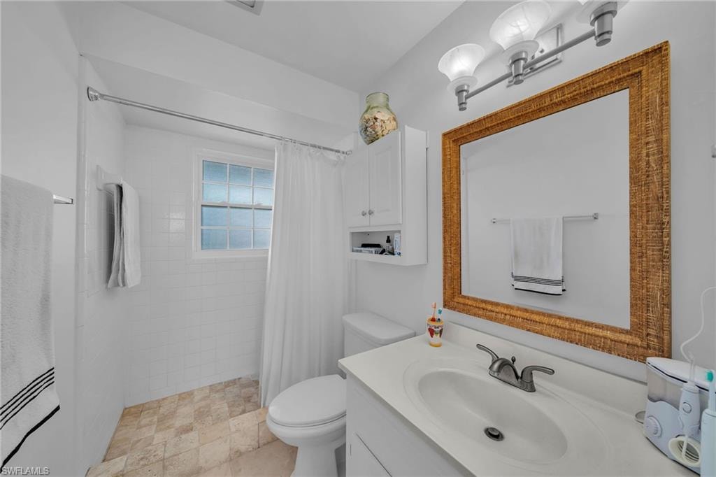 Bathroom featuring a vanity with an integrated sink, a large framed mirror, and a white tiled shower with a window