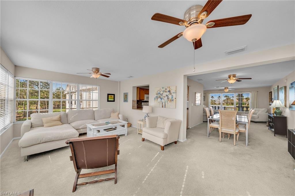 Bright living area featuring expansive windows, neutral carpeting, and multiple ceiling fans