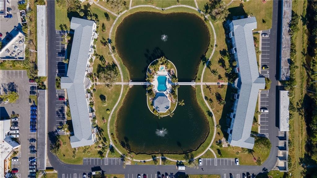 Aerial view of a residential complex featuring two multi-story buildings, a central lake with water features, a swimming pool, and dedicated parking areas
