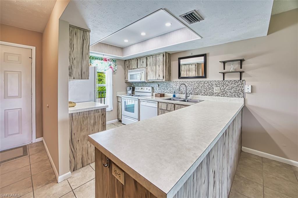 Kitchen with a textured ceiling, white appliances, light tile patterned floors, light countertops, and open shelves