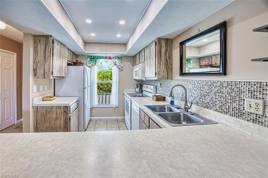 Kitchen with light countertops, white appliances, a tray ceiling, recessed lighting, and light tile patterned floors
