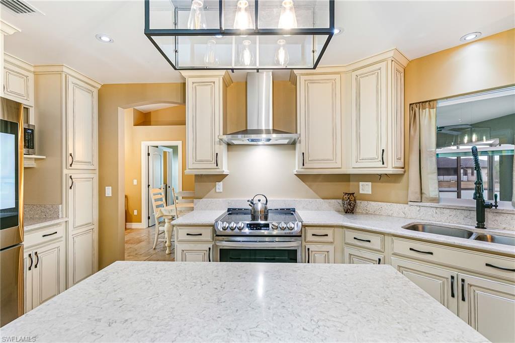 Kitchen featuring white perimeter cabinetry with dark hardware, a stainless steel range with a coordinating vent hood, and a dual basin undermount sink with a black high-arc faucet - Virtually Edited Image