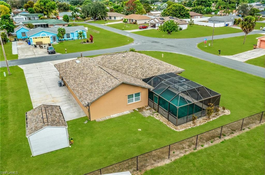 Spacious property featuring a screened-in swimming pool, a concrete driveway, a separate storage shed, lush green lawn, and a perimeter fence - Virtually Edited Image