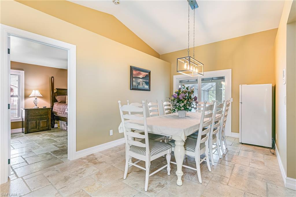 Dining area featuring a vaulted ceiling, rectangular pendant light fixture, and stone tile flooring - Virtually Edited Image