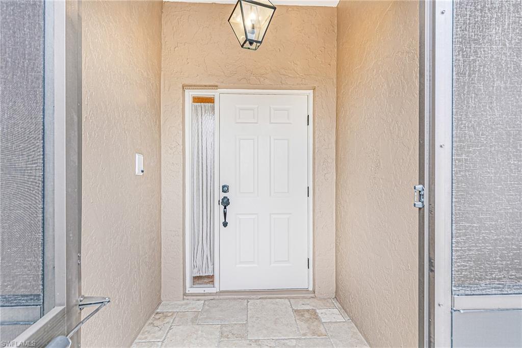 Entryway featuring a paneled white door with black hardware, a frosted glass sidelight, and an overhead lantern-style light fixture - Virtually Edited Image