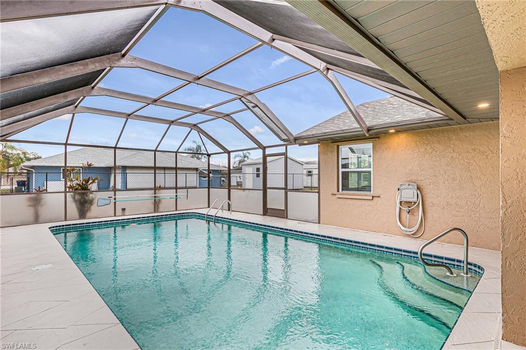 Screened enclosure featuring a rectangular pool with integrated steps, metal handrails, and a perimeter of white tile decking - Virtually Edited Image
