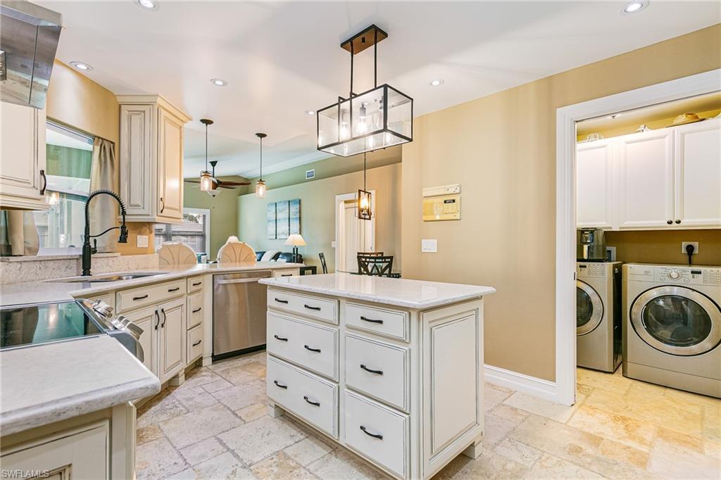Kitchen featuring an island with built-in drawers, cream-colored cabinetry, stone-finish flooring, recessed lighting, and a separate laundry area with stacked appliances and upper cabinetry - Virtually Edited Image