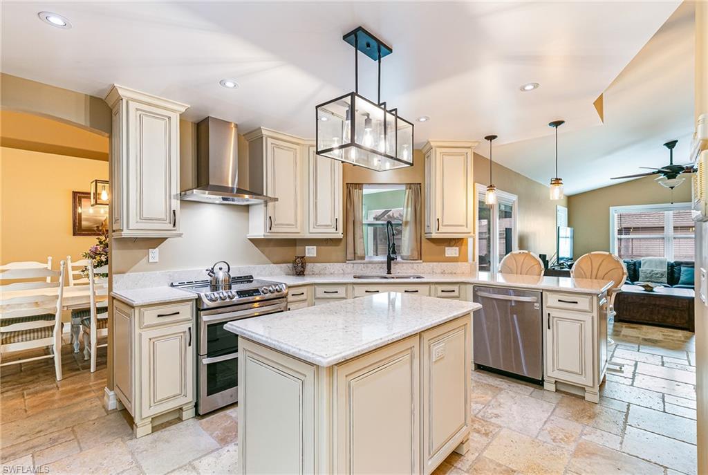 Spacious kitchen featuring an island with a light-toned countertop, cream cabinetry, stainless steel appliances, and stone flooring - Virtually Edited Image