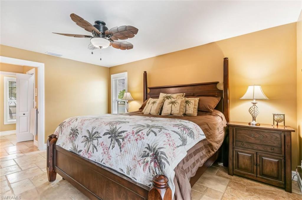 Bedroom featuring tile flooring, a ceiling fan with light fixture, and window with plantation shutters - Virtually Edited Image