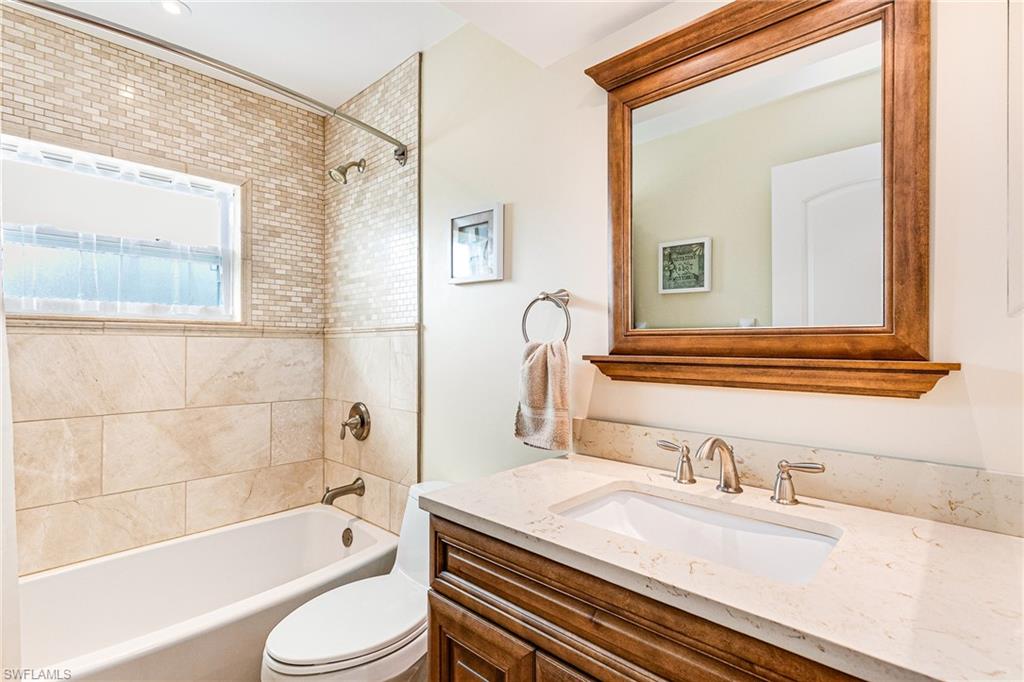 Bathroom featuring a built-in bathtub, a window, and extensive tile work - Virtually Edited Image