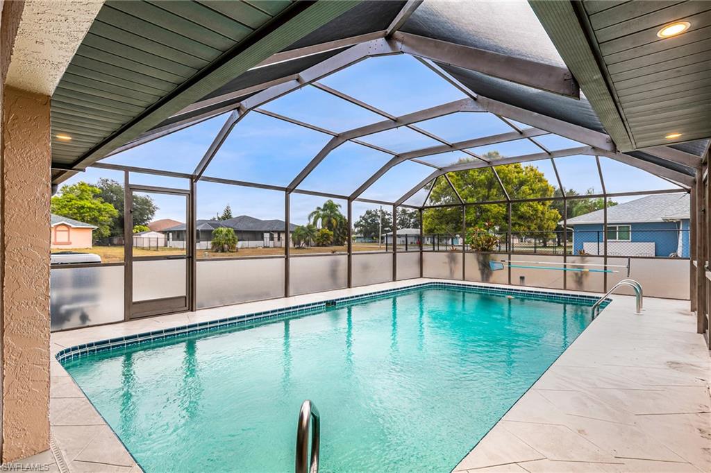 Screened-in pool enclosure featuring a rectangular swimming pool with blue tile trim, a spacious concrete pool deck, and recessed lighting in the patio ceiling - Virtually Edited Image