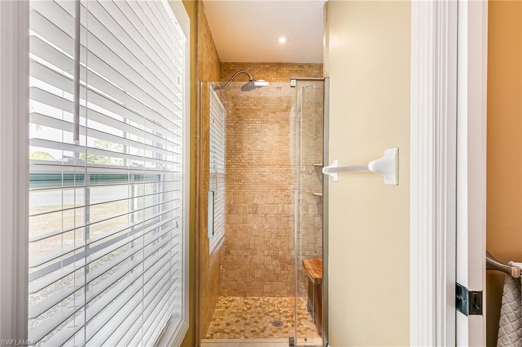 Walk-in shower featuring glass enclosure, stone tile walls, pebble floor, and integrated wooden bench - Virtually Edited Image