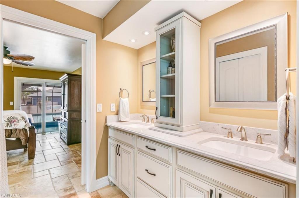 Bathroom vanity featuring dual under-mount sinks, light-toned stone countertop, and white cabinetry - Virtually Edited Image
