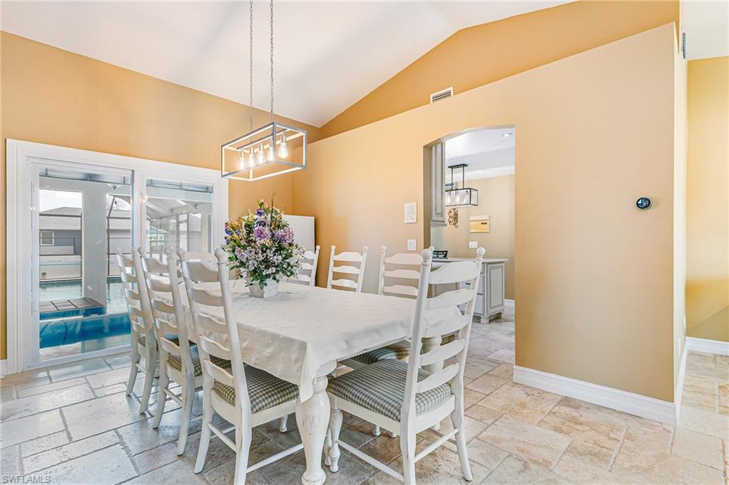 Dining area featuring vaulted ceilings, floor-to-ceiling sliding glass doors, a contemporary chandelier, and tile flooring - Virtually Edited Image