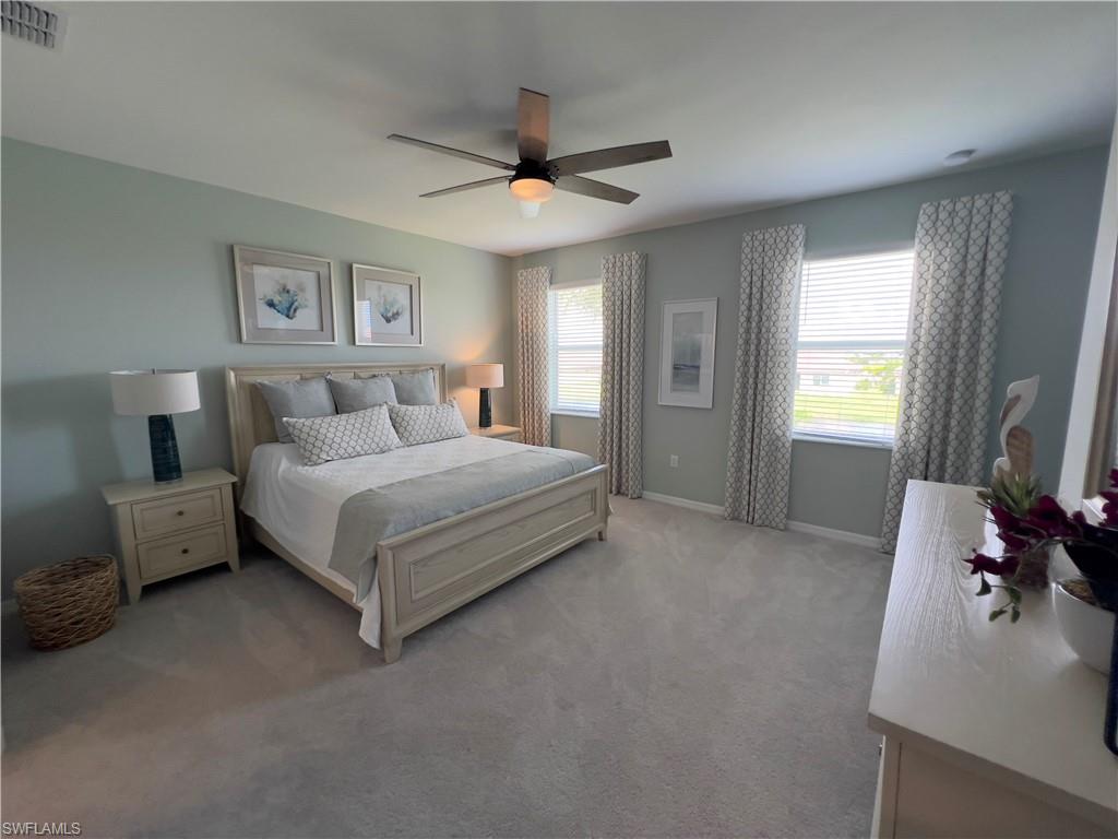 Bedroom with ceiling fan, light carpet, and multiple windows