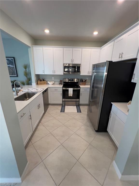 Kitchen with light tile patterned floors, stainless steel appliances, white cabinetry, and sink