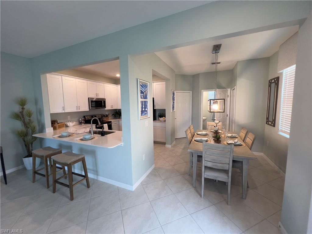 Kitchen with white cabinetry, decorative light fixtures, stainless steel appliances, kitchen peninsula, and sink