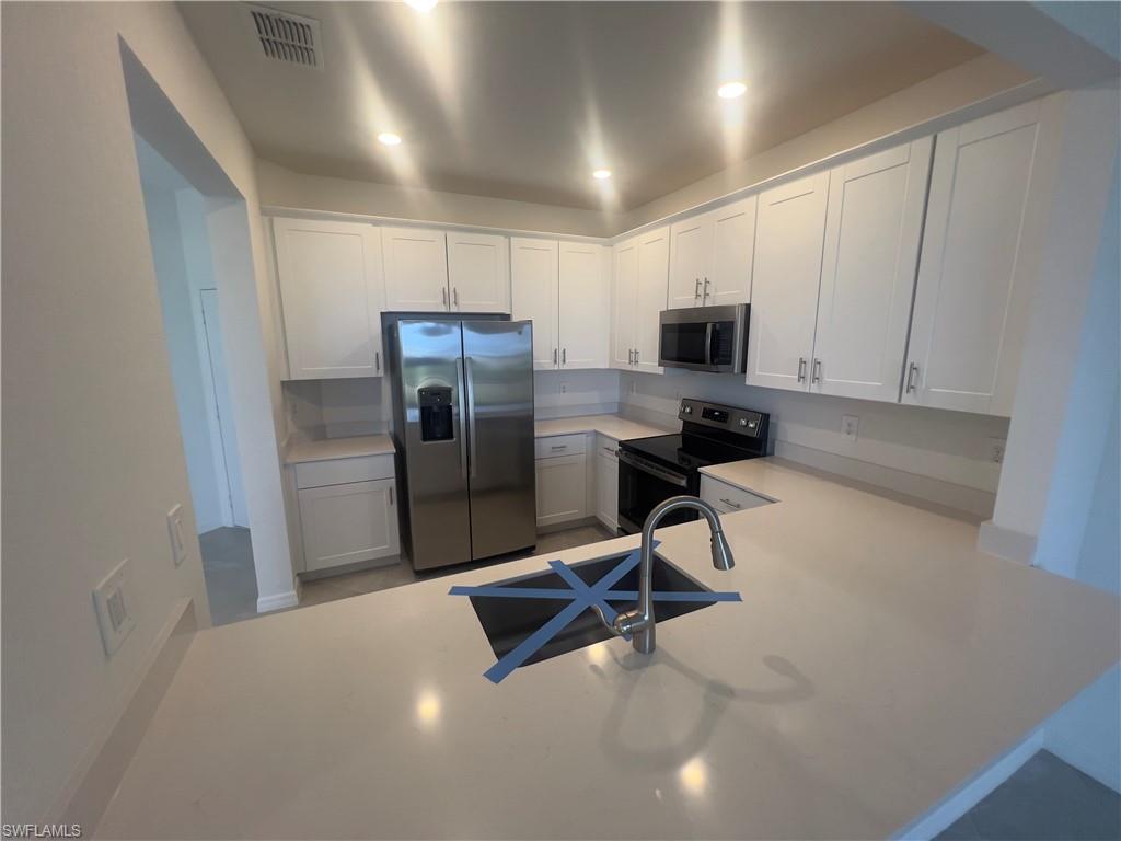 Kitchen featuring kitchen peninsula, stainless steel appliances, white cabinetry, and sink