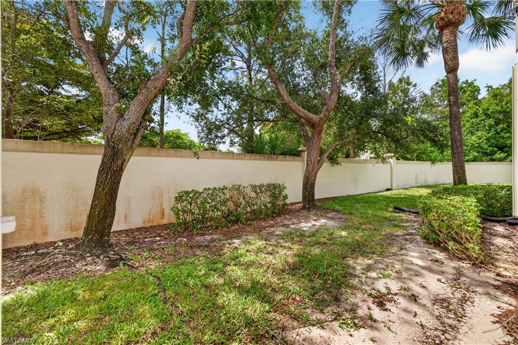 Landscaped outdoor area featuring a stucco privacy wall, mature trees, manicured shrubs, and a grassy lawn