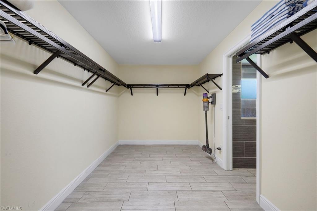 Spacious closet featuring wall-mounted shelving, wood-finish tile flooring, a white trim baseboard, and ceiling-mounted lighting