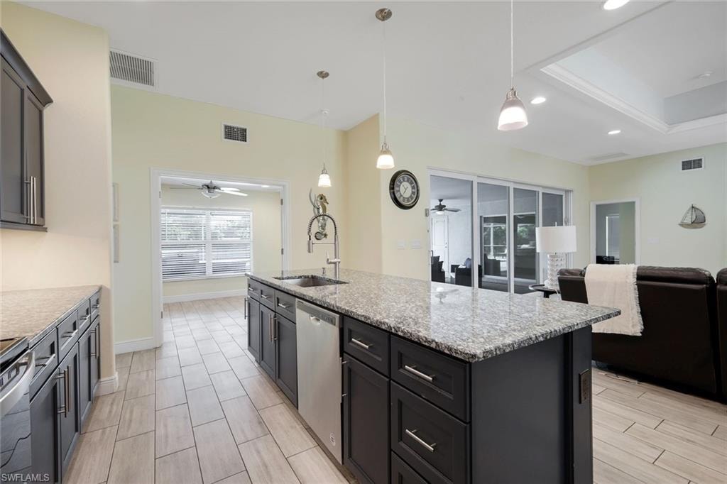 Modern kitchen featuring a central island with a sink, stainless steel appliances, dark cabinetry, and light-toned tile flooring