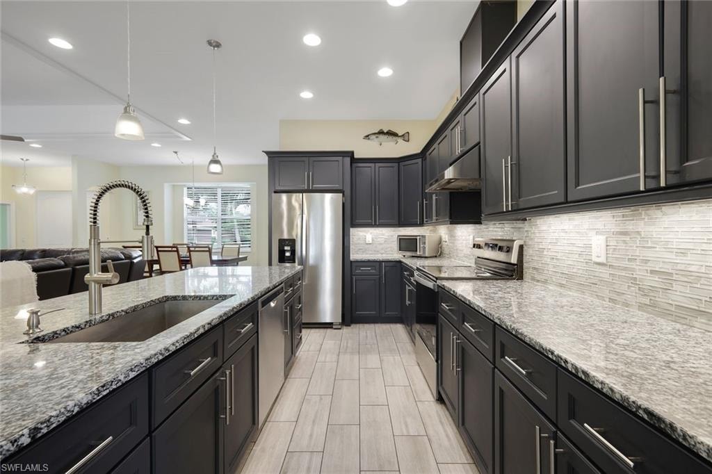 Modern kitchen featuring dark cabinetry, stainless steel appliances, and a central island with a built-in sink