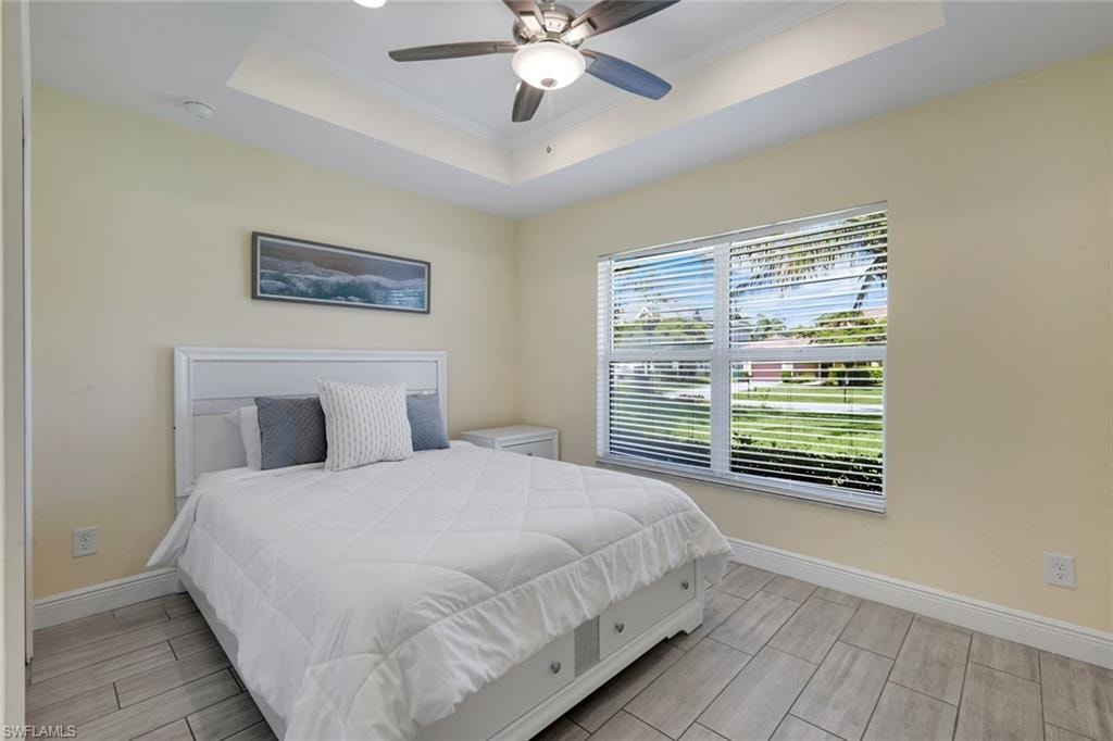 Recessed tray ceiling with a built-in ceiling fan, expansive window with white blinds, neutral wall paint, and light-toned tile flooring