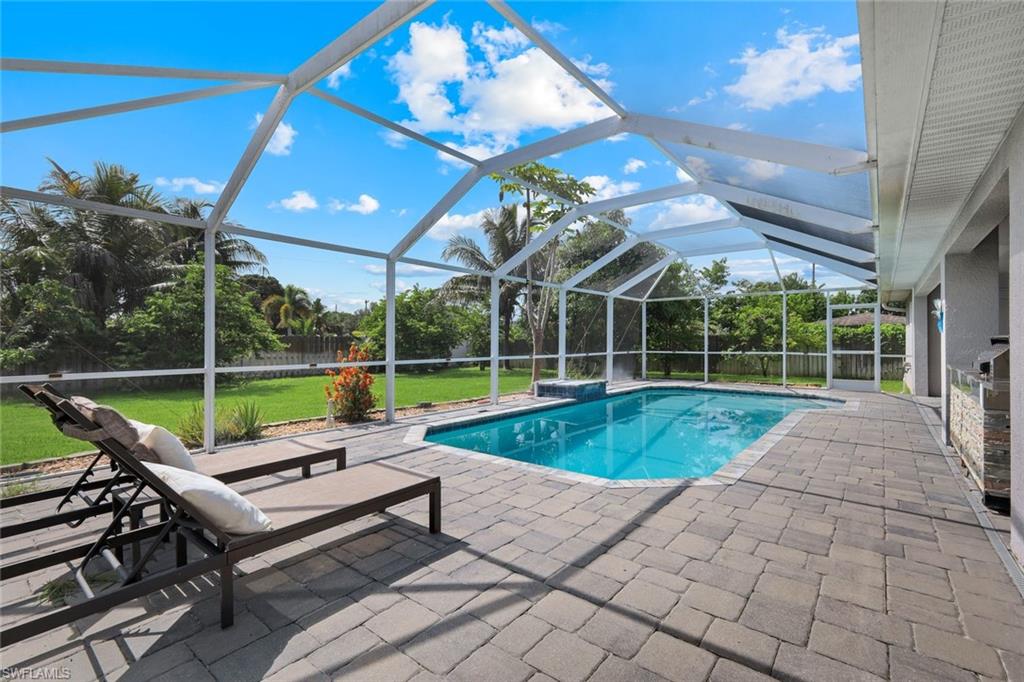 Screened-in pool area featuring a rectangular swimming pool with integrated spa, paver deck, and a covered outdoor kitchen space with stone accents