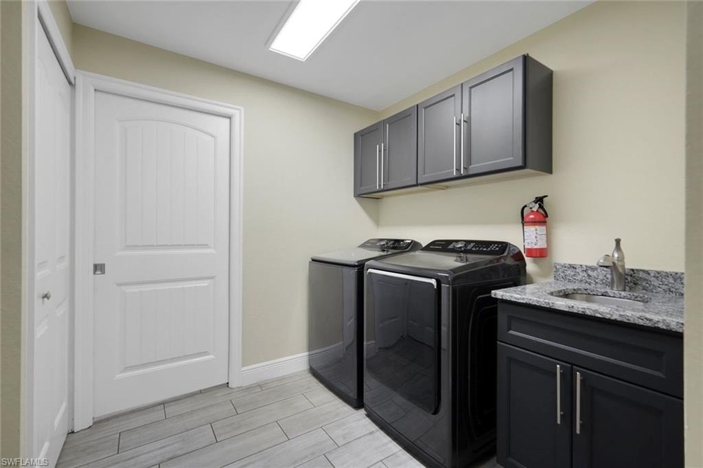 Utility space featuring wood-finish tile flooring, a white paneled door, dark cabinetry with brushed nickel hardware, and a vanity with an undermount sink and stone countertop