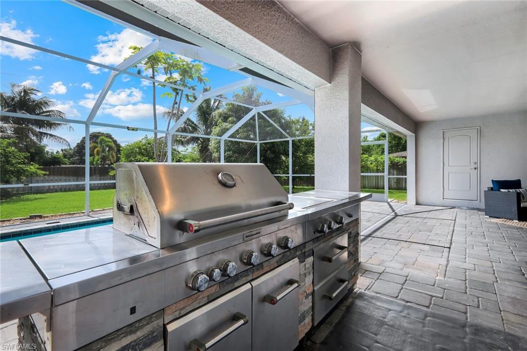 Expansive screened patio featuring a built-in stainless steel outdoor kitchen, stone veneer accents, and paver flooring
