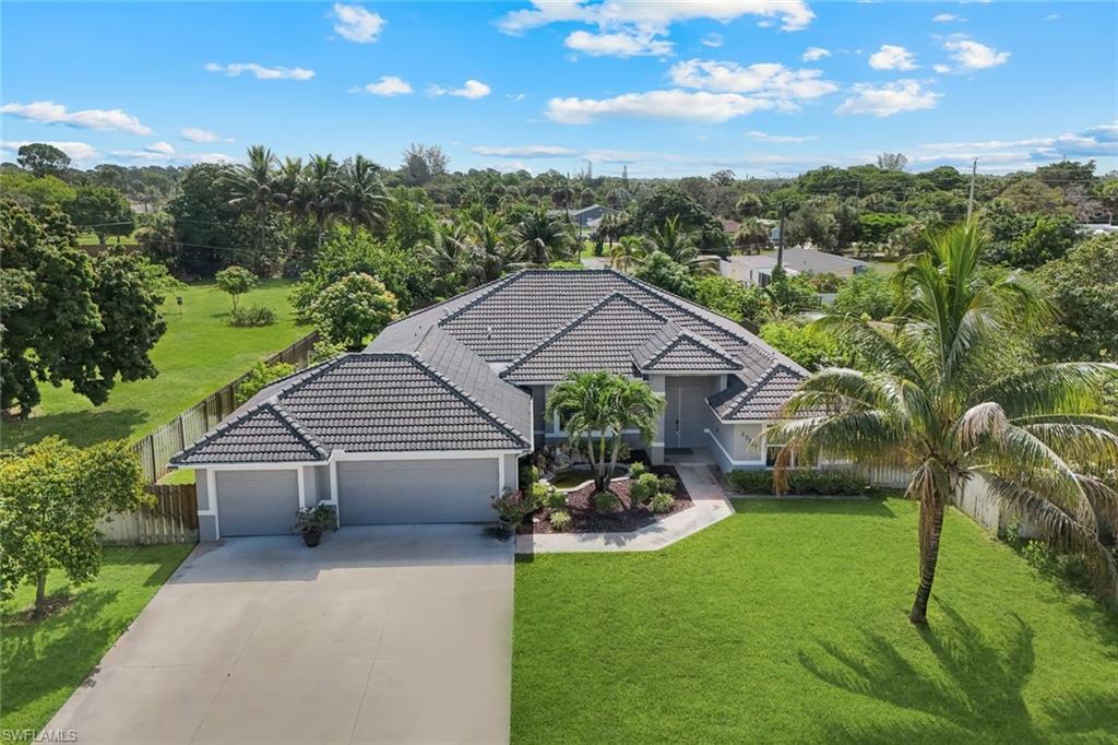 Light gray exterior with a dark tile roof, featuring a two-car garage, mature landscaping, and an expansive green lawn