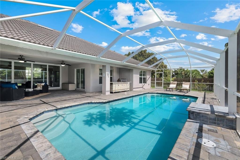 Screened lanai featuring a swimming pool with integrated steps, paver decking, and an outdoor kitchen