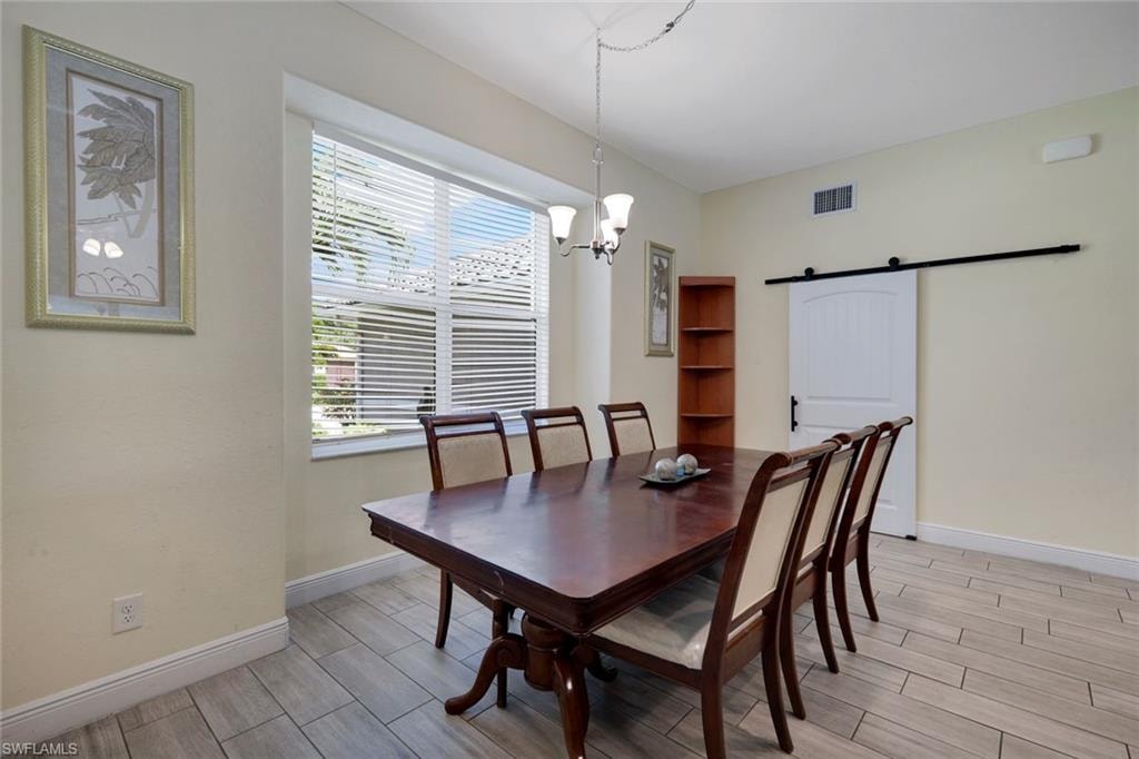 Dining area featuring wood-finish tile flooring, a window with horizontal blinds, and a white barn door on a black track