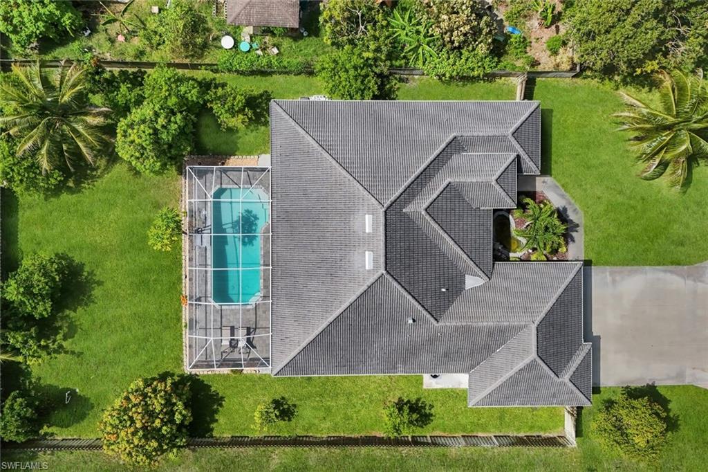 Overhead view showcasing the home's multi-gabled roofline, screened pool enclosure, mature landscaping, and concrete driveway