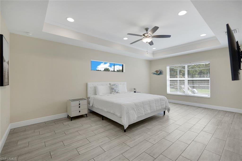 Recessed lighting and a ceiling fan illuminate this room featuring a tray ceiling