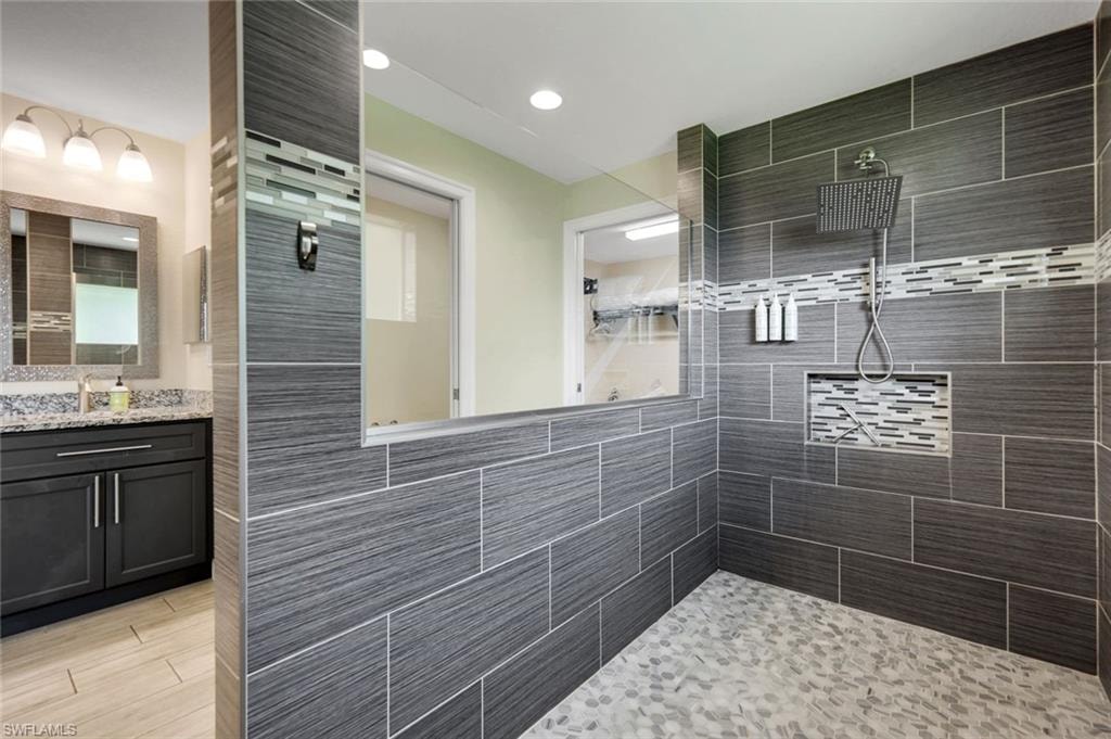 Walk-in shower featuring large format gray wall tile, a linear mosaic accent band, a built-in shower niche, and pebble-style floor tile