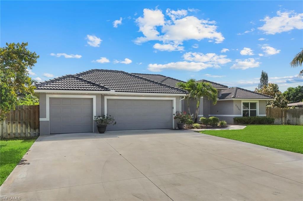Exterior stucco residence featuring a dark tile roof, a two-car garage, concrete driveway, and a manicured front lawn