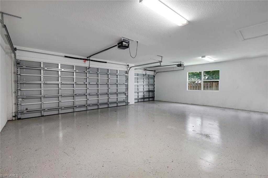 Spacious garage featuring two overhead doors, an automatic garage door opener, durable epoxy flooring, overhead fluorescent lighting, and a transom window