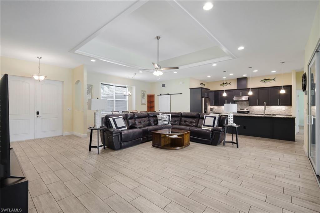 Spacious open-concept living area featuring wood-finish flooring, a tray ceiling with recessed lighting, and a kitchen with dark cabinetry, stainless steel appliances, and pendant lighting