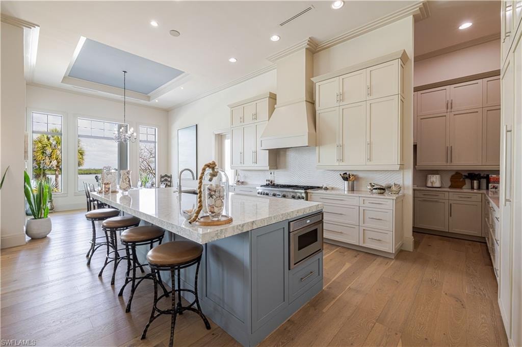 Kitchen featuring a large central island with seating, light-toned wood-finish flooring, white cabinetry, integrated stainless steel appliances, and a coffered ceiling